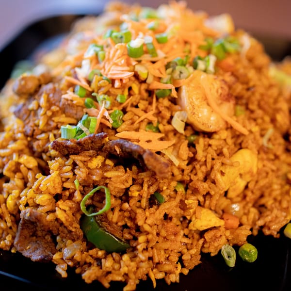 Hibachi Boy's fried rice with beef, shrimp, carrots, and green onions on a black plate.