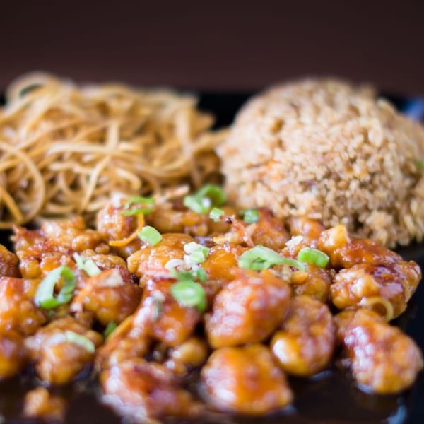 Hibachi Boy's General Tso's chicken with fried rice and crispy noodles on a black plate.