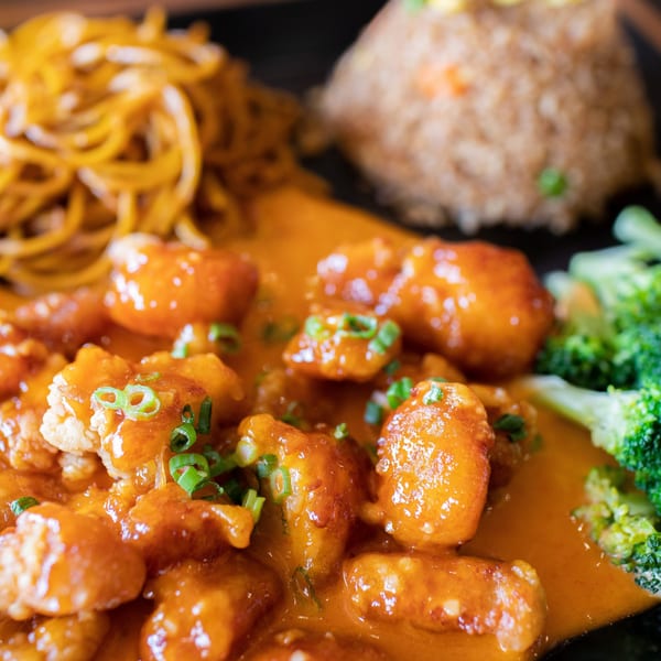 Hibachi Boy's orange chicken with noodles, fried rice, and broccoli on a black plate.